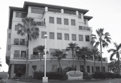 Black and white photo of five-story building surrounded by palm trees with sign in front reading "Ugland House."