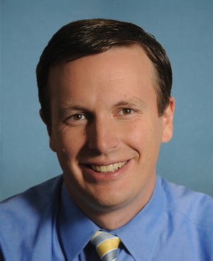 Head and shoulders shot of smiling young man with short dark hair, wearing blue shirt and tie.