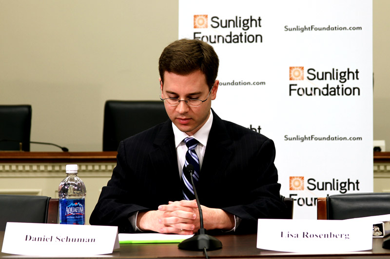 Daniel Schuman sitting and looking over remarks with Sunlight Foundation banner in the background.