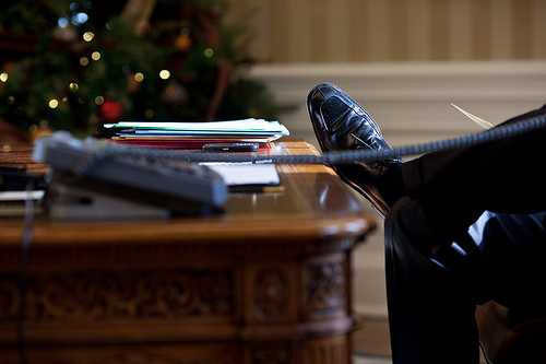 President Barack Obama leans back in his chair while on the phone in the Oval Office.