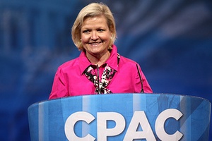 Image of blonde woman in pink shirt with scarf speaking behind a podium labelled CPAC