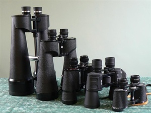 A set of 5 different binoculars of varying sizes arranged on table.
