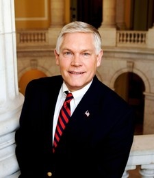 Image of Pete Sessions, smiling white haired man in dark suit and red rep tie, with Cannon rotunda in background