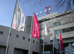 Photo of modernistic white building with four white and pink flags in front and stylized T logo on top