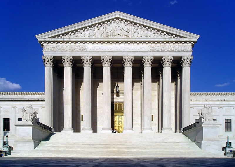 A view of the west facade of the U.S. Supreme Court building, full of grand columns set to a blue sky background.