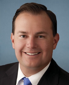 Head and shoulders shot of Sen. Mike Lee, smiling white man with dark brown hair, dark suit, blue tie