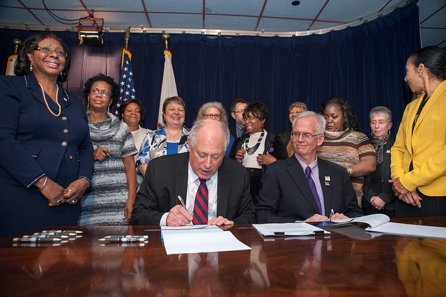 Gov. Pat Quinn at table, signing documents surrounded by a group of women, standing