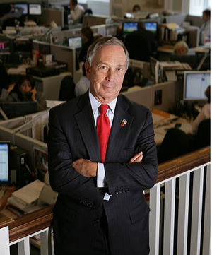 Former New York City Mayor Michael Bloomberg standing with red tie and arms crossed.