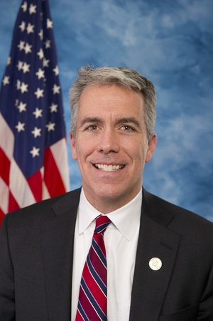 Head and shoulders shot of Rep. Joe Walsh, salt-and-pepper haired man in dark suit, white shirt, red tie with U.S. flag over his right shoulder