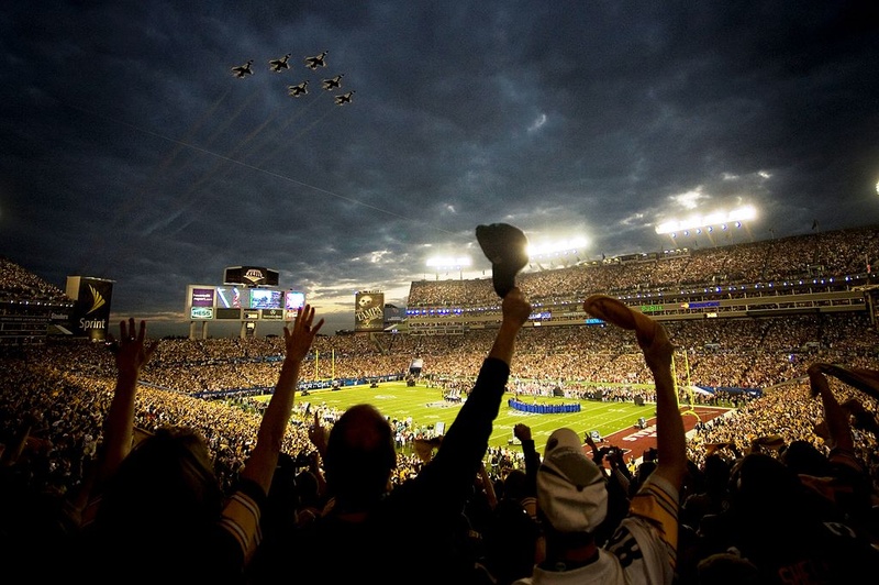A stadium of cheering fans with planes flying in a darkened sky overhead.