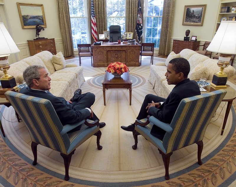 George W. Bush and Barack Obama sit in chairs in the Oval Office.