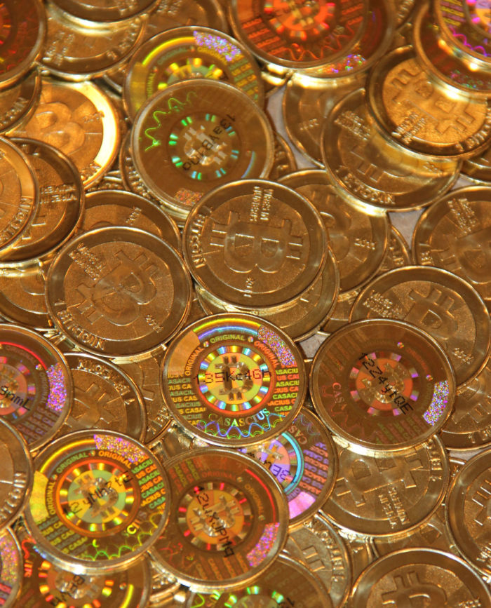 Photos shows pile of 1BTC-denominated brass coins, with the bitcoin logo, production year, the text "Vires In Numeris", with the tamper-evident holographic sticker on the reverse. Printed on the sticker is a portion of the digital coins' public address, for verification of the coin's value. Beneath the holographic sticker lies a private cryptographic key, used to redeem the coin's value, and move the bitcoins contained by the coin into the owner's private wallet. Removing the holographic sticker leaves a hexagon pattern, and indicates to any future owners that the digital Bitcoin originally loaded on the coin have likely been removed. Date Source https://www.casascius.com/photos.aspx Author Mike Cauldwell Permission (Reusing this file) https://www.casascius.com/photos.aspx